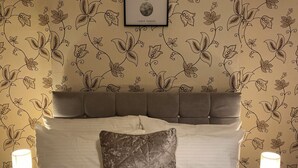 A neatly made bed with a quilted pillow, a framed picture of lunar phases, and a floral wallpaper pattern. - Remarkable 3-bed House in Liverpool (Liverpool)