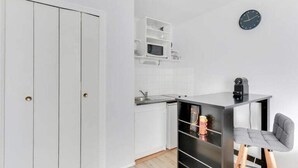 Een kleine keuken met witte kastjes, een magnetron en een zwart aanrecht.