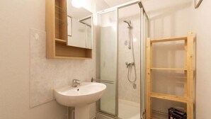 Een badkamer met een douchecabine van glas, een witte wastafel en een houten plankunit.