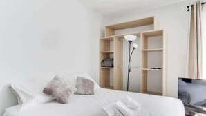 Een opgemaakt bed met kussens, een bedlampje en een televisie op een voetstuk.