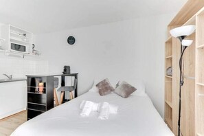 Ett modernt hotellrum med en välordnad säng, ett litet pentry och en garderob i trä.