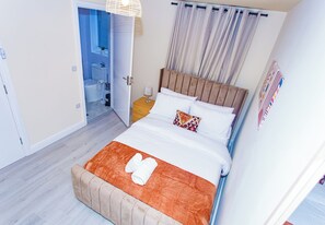 A hotel room with a bed, a nightstand, a window with curtains, and a view of the bathroom.