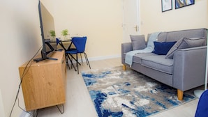 Un espacio habitable pequeño con un escritorio de madera, un sofá gris y una silla azul.
