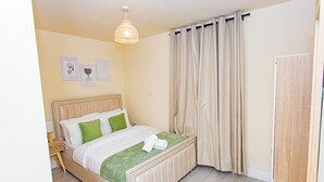 Una cama bien tendida con un plaid verde, una lámpara de noche y un aplique de pared.