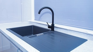 Una cocina con un lavamanos negro y grifo, una encimera blanca y un ventanal sobre el lavamanos.