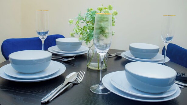 Una mesa de comedor dispuesta con platos blancos, tazones, cubiertos y un vaso de agua.