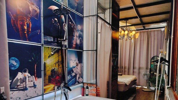 A bathroom with a large bathtub, a shower, and a window with space-themed artwork.