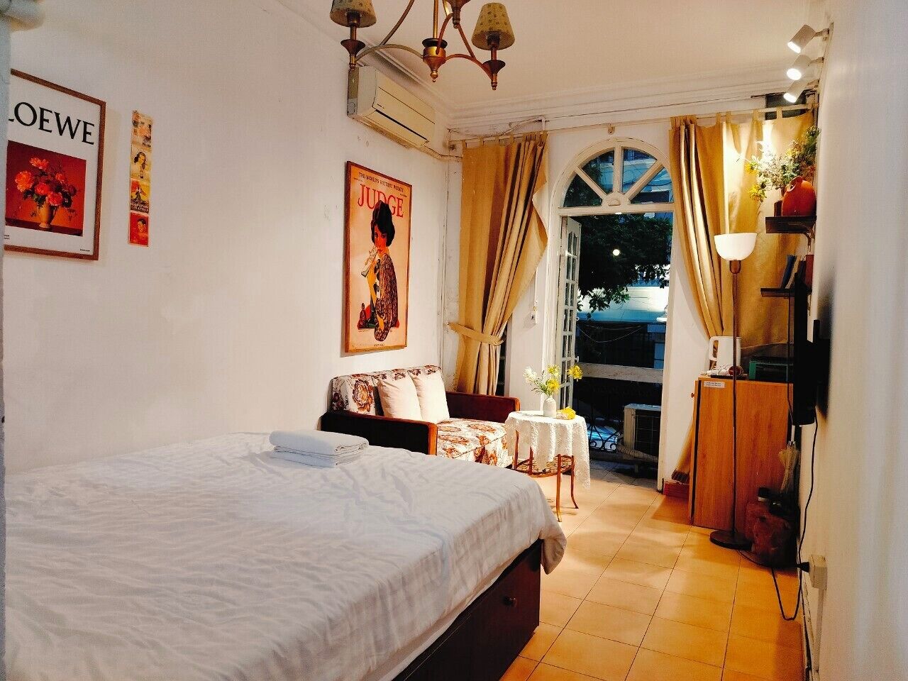 Een slaapkamer met een bed, een tafeltje met bloemen, een bank en een bureau met een lamp.