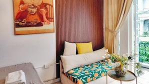 A bedroom with a wooden headboard, a bed with patterned bedding, a small table with a vase of flowers, and a painting on the wall.