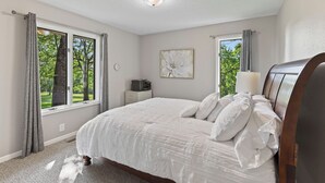 A bedroom with a large bed, a bedside table, a lamp, and a window with curtains.