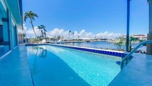 A clear blue pool with a blue tiled edge, surrounded by palm trees and a view of a marina with boats. - Paradise Found! Luxurious Private Waterfront Vacation Home with Pool.  (Punta Gorda)