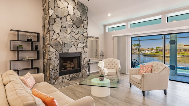 A modern living room with a stone fireplace, a glass coffee table, and a view of a swimming pool. - Paradise Found! Luxurious Private Waterfront Vacation Home with Pool.  (Punta Gorda)