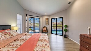 A bedroom with a large bed, a chair, a dresser, and a view of a pool through glass doors. - Paradise Found! Luxurious Private Waterfront Vacation Home with Pool.  (Punta Gorda)