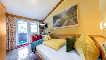 A cozy bedroom with a wooden bed, a television, a painting of a mountain landscape, and a window with curtains.