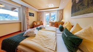 Quarto de hotel com duas camas, vista para montanhas, escrivaninha com cadeira e janela com cortinas.