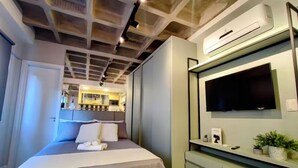 Ett modernt hotellrum med en säng, en TV som är monterad på väggen och en liten köksdel.