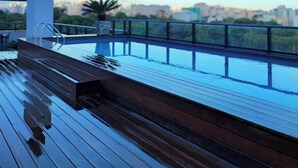 En pool på taket med trädäck och ett metallräcke, med utsikt över stadsbilden.