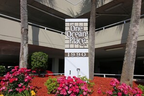 A building with a sign reading "One Ocean Place 1990" surrounded by red mulch and pink flowers.