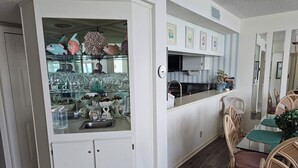 A modern kitchen with a glass-fronted cabinet, a dining area with wicker chairs, and a kitchen island with a sink.