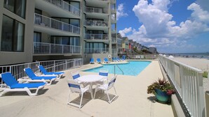 A poolside area with lounge chairs and a table, overlooking a beach and a hotel building.