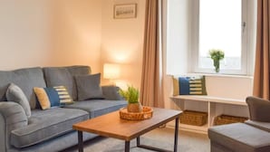 A living room with a grey sofa, a wooden coffee table, and a view of the sea through a window. - Stunning Sea Views in Central Burntisland (Burntisland)