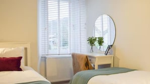 A bedroom with two beds, a window with blinds, a radiator, a desk with a mirror, and a potted plant. - Stunning Sea Views in Central Burntisland (Burntisland)
