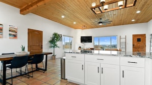 A spacious kitchen with white cabinets, a wooden ceiling, and a large island with a sink.