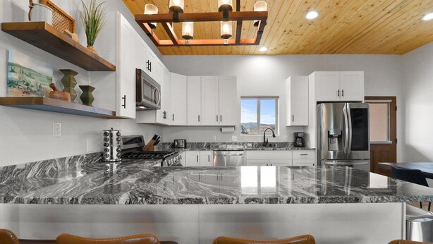 A modern kitchen with white cabinets, a granite countertop, and a stainless steel refrigerator.