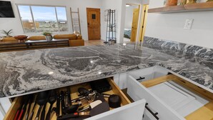 A modern kitchen with a marble countertop, a built-in drawer with utensils, a wooden door, and a view of the outdoors.
