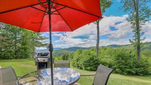 A patio with a glass table, chairs, and a red umbrella. - New Hampshire vacation getaway with gorgeous mountain views—ski, hike, swim! (Thorton)