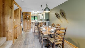 A dining area with wooden chairs and a table set for six, a kitchen in the background, and a large pendant light above the table. - New Hampshire vacation getaway with gorgeous mountain views—ski, hike, swim! (Thorton)