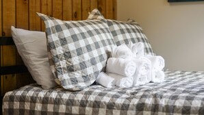 A bed with a checkered bedspread, two pillows, and a stack of rolled towels. - New Hampshire vacation getaway with gorgeous mountain views—ski, hike, swim! (Thorton)