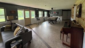 A spacious living area with a gray sofa, a wooden coffee table, and a dining table with chairs. There are large windows providing natural light and a view of the outdoors. - 5min to Breweries and 25min to Tail of the Dragon. Pool table + pet friendly! (Andrews)
