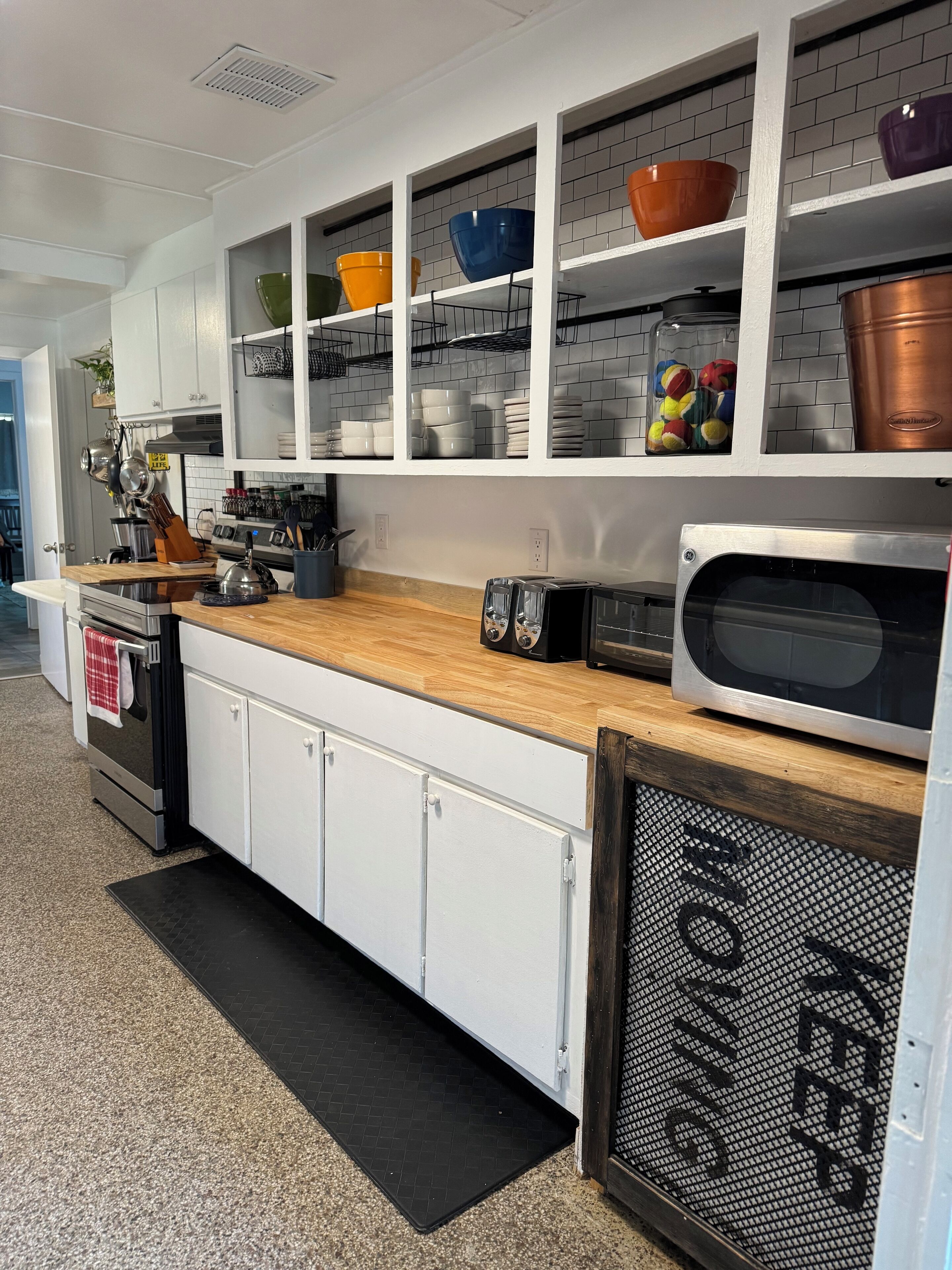 A modern kitchen with white cabinets, a wooden countertop, and a built-in microwave.