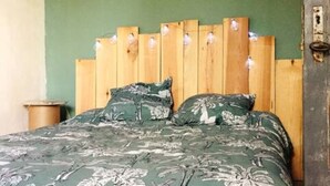 Un lit avec une tête de lit en bois et deux oreillers, un mur vert et une petite poubelle.