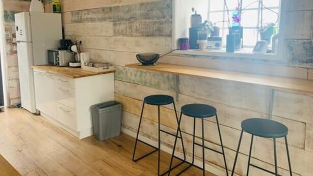 Une cuisine avec un mur en bois, une fenêtre, un réfrigérateur, un évier et trois tabourets.