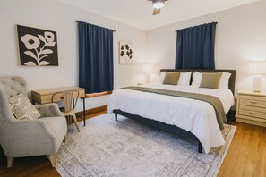 A bedroom with a bed, bedside tables, a desk, a chair, and two wall-mounted lamps.