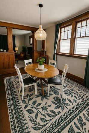 A dining area with a round wooden table, white chairs, a woven pendant light, and a patterned rug.