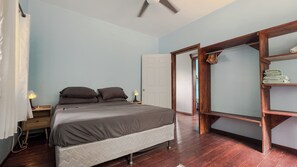 A bedroom with a bed, bedside lamps, a wooden wardrobe, and a door leading to another room. - House On The Hill majestic ocean view walking distance to beach and restaurants (Roatan)
