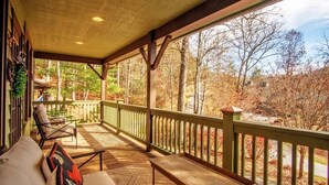 A covered porch with wooden furniture and a view of a forest. - Fern Cliff - A cozy retreat in Cashiers (Cashiers)