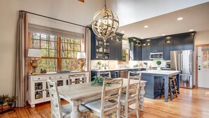A spacious kitchen with dark cabinets, a wooden dining table, and a large window with curtains. - Fern Cliff - A cozy retreat in Cashiers (Cashiers)