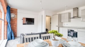 Una cocina moderna con armarios blancos, horno integrado y un comedor con una mesa de madera para cuatro.