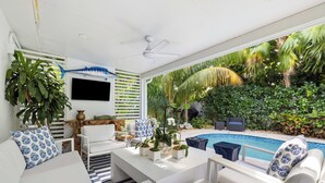 A modern living room with a pool view, white furniture, and tropical plants.