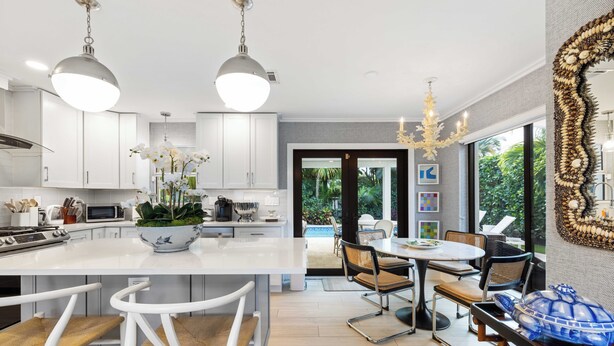 A modern kitchen with white cabinets, a central island, and a dining area with a round table and chairs.