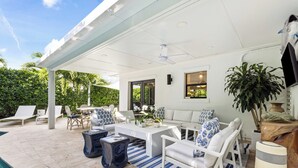 A covered outdoor patio with white furniture, a pool, and a ceiling fan.