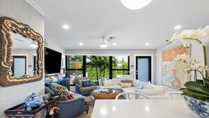 A modern living room with a large mirror, sofas, a dining table, and a view of the outdoors.