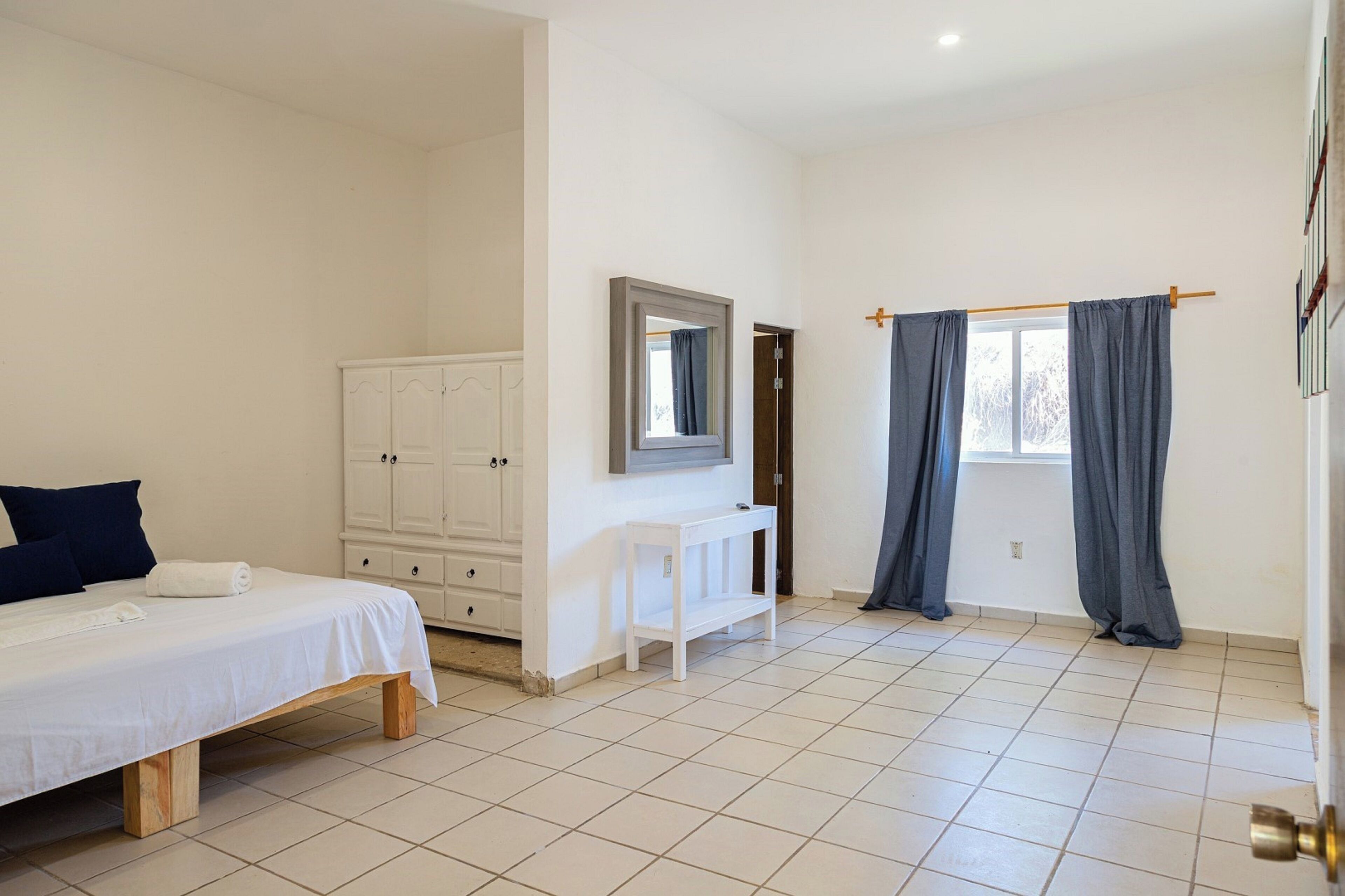 Un dormitorio con cama, armario, tocador, espejo y ventana con cortinas.