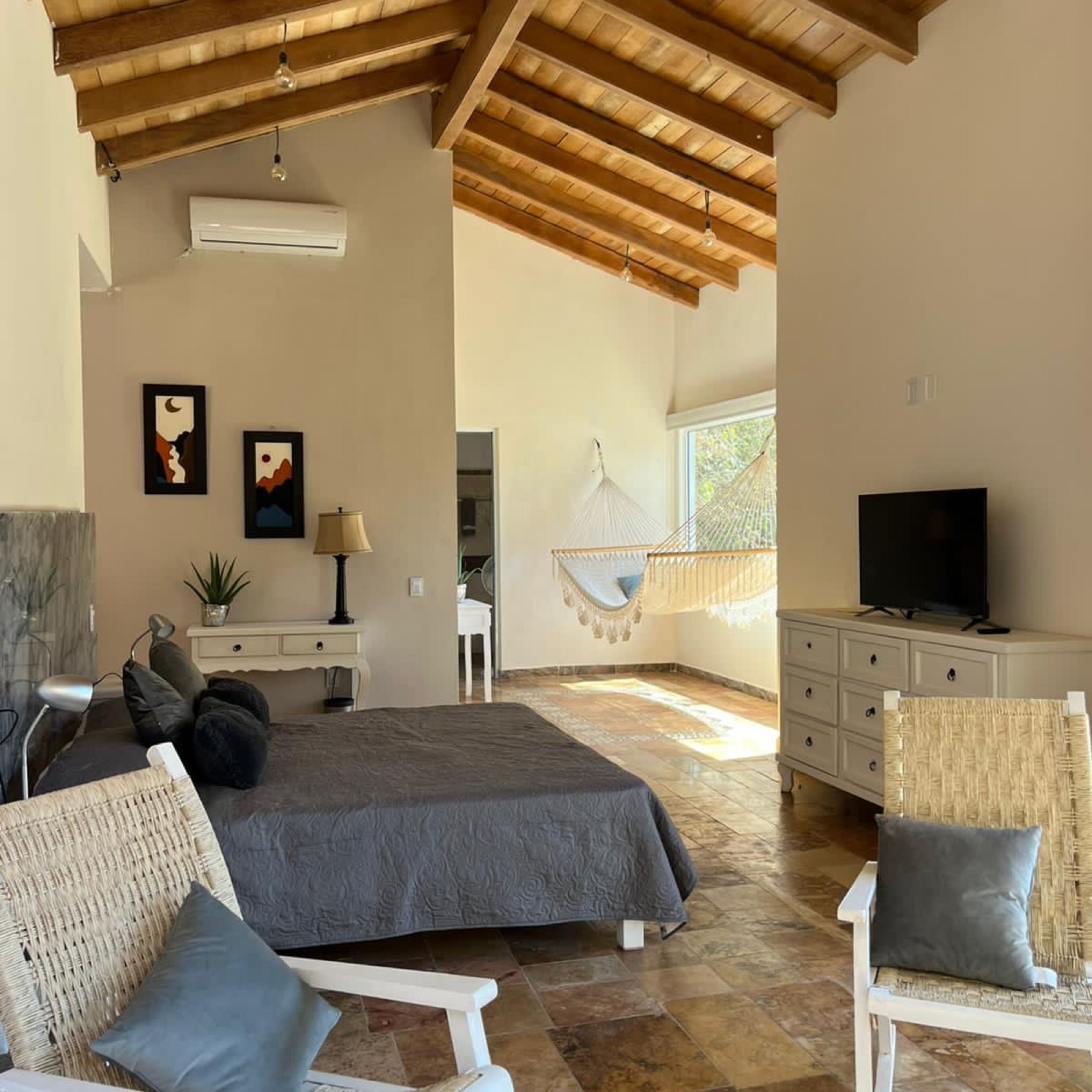 Un dormitorio amplio con una cama grande, televisión, escritorio y una hamaca.