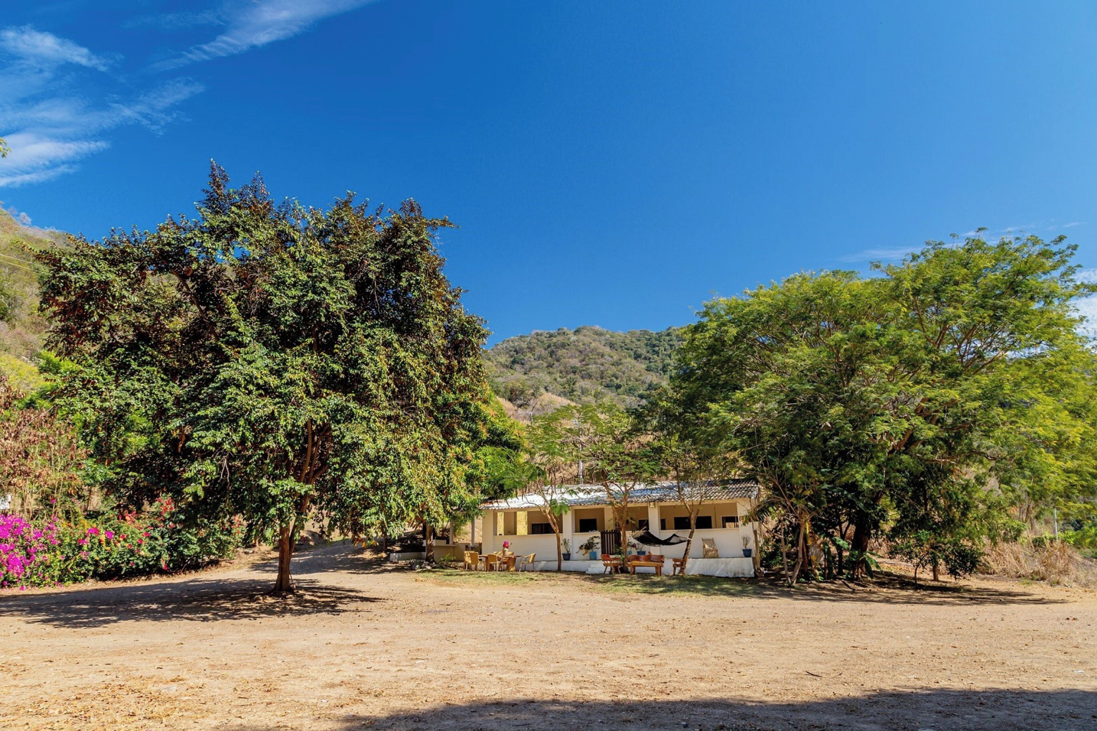 A rustic building with a flat roof, surrounded by trees and hills.