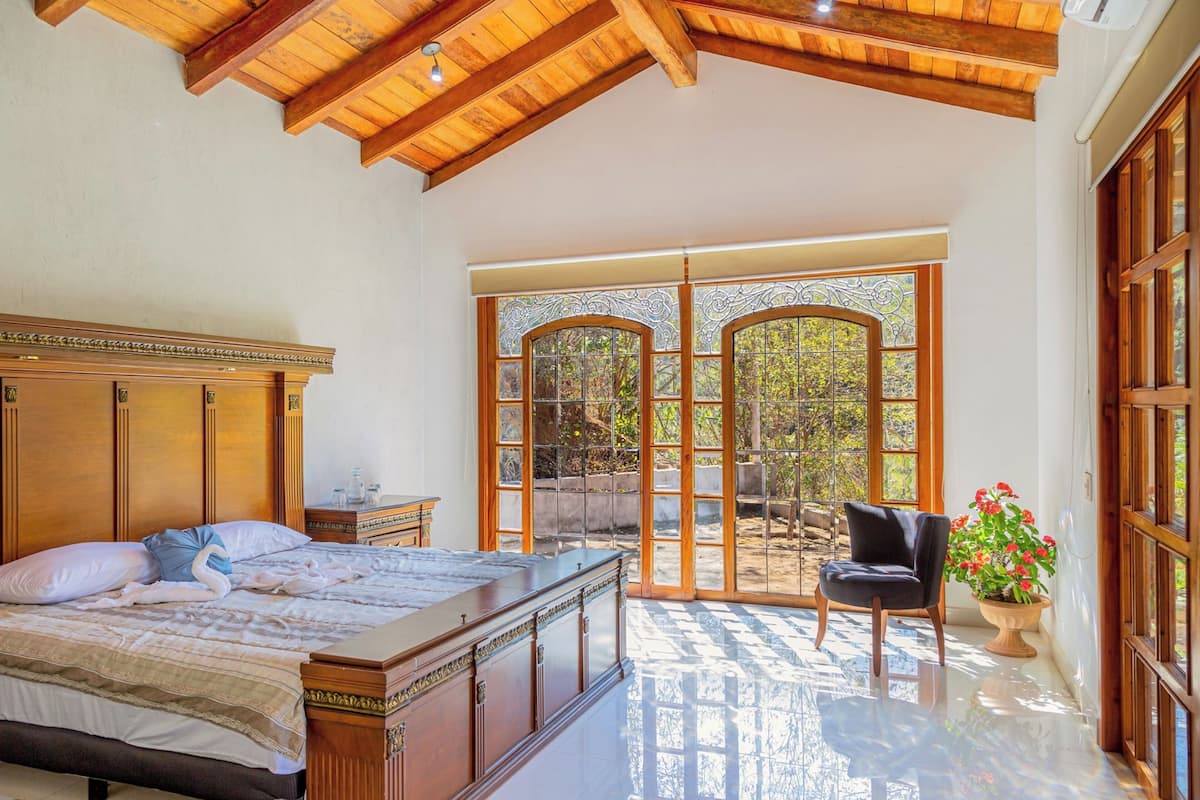 A bedroom with a large bed, wooden headboard, and a view through a glass door to an outdoor area.